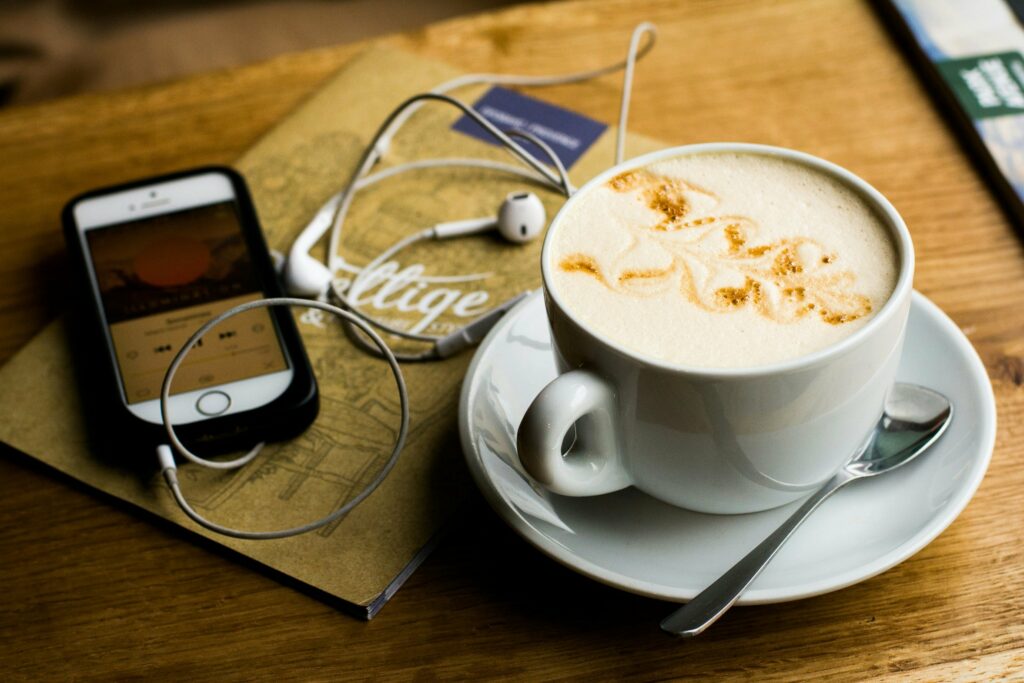 Cappucino and a phone showing a podcast on the screen, with ear buds.