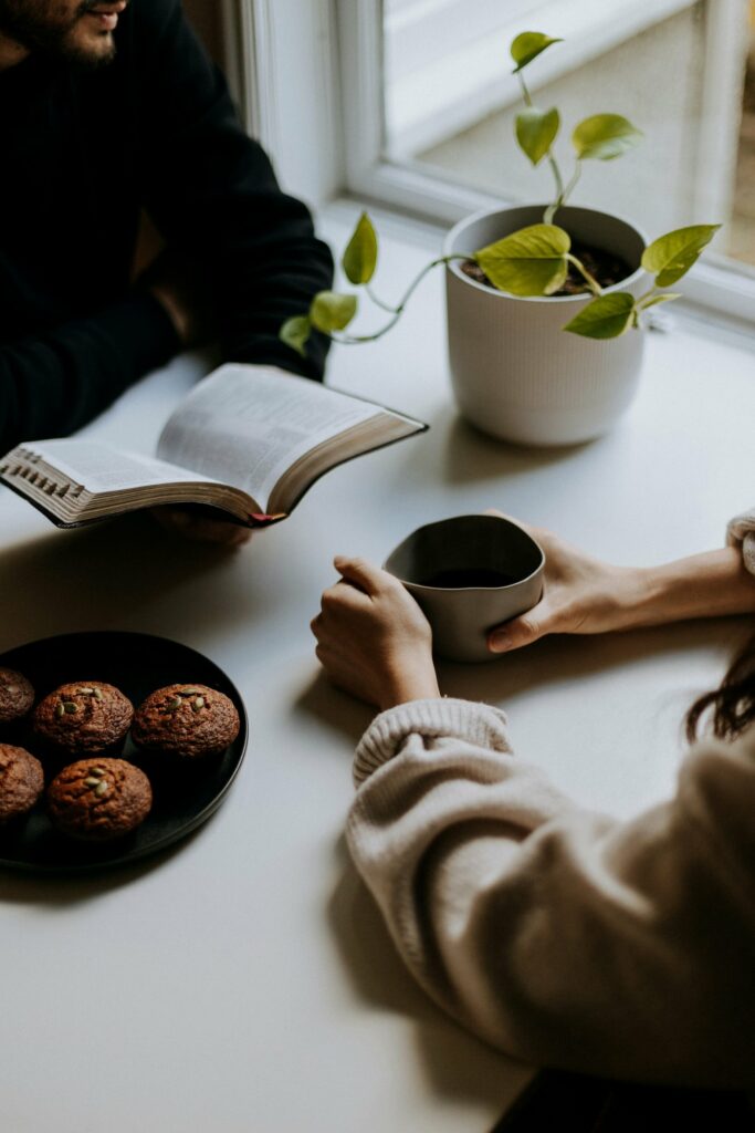 Two women sitting at a table, one holding a bible and the other a cup of coffee.