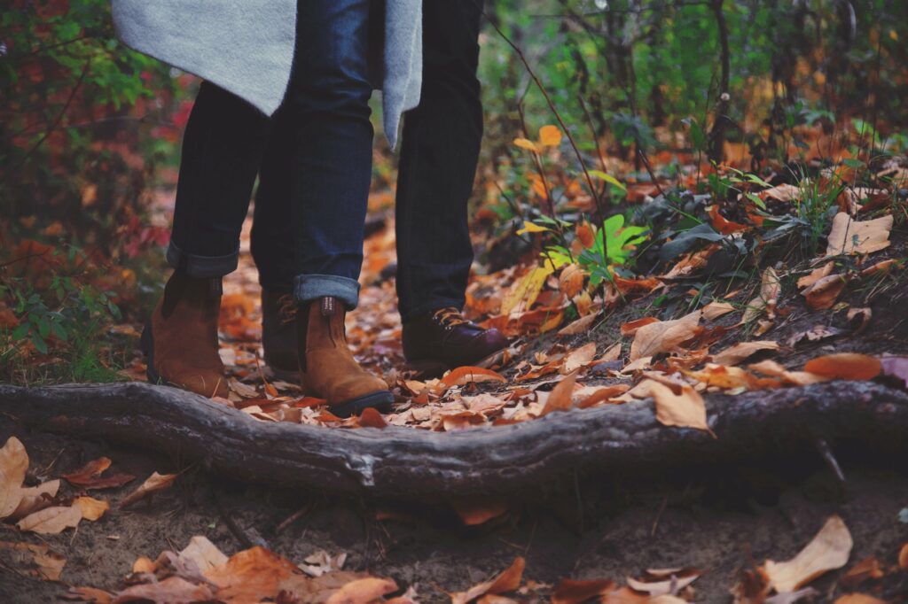 Man and woman's feet on a trail covered in leaves.